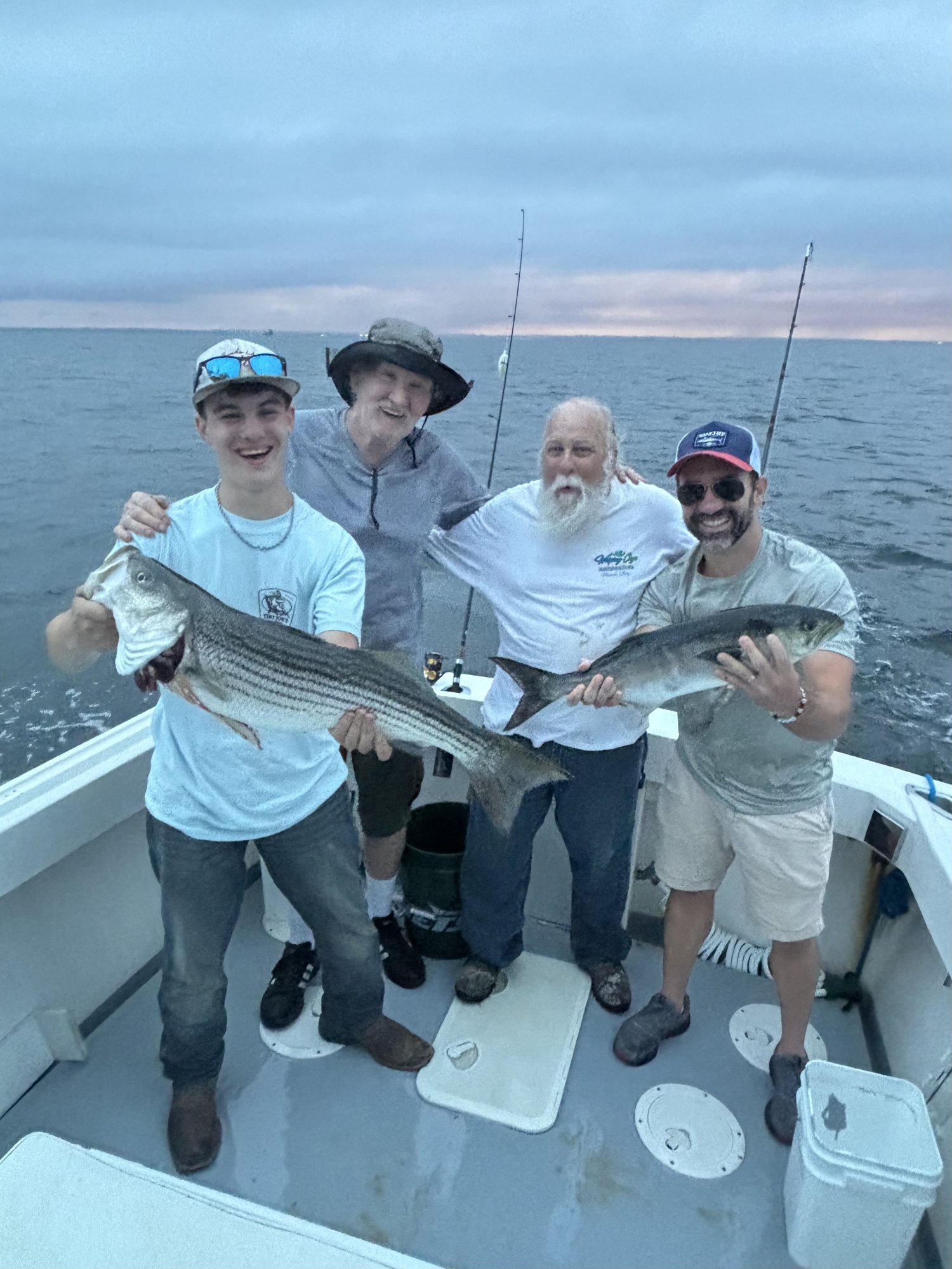 Four anglers holding striped bass at dusk on the Long Island Sound aboard the Christina M II