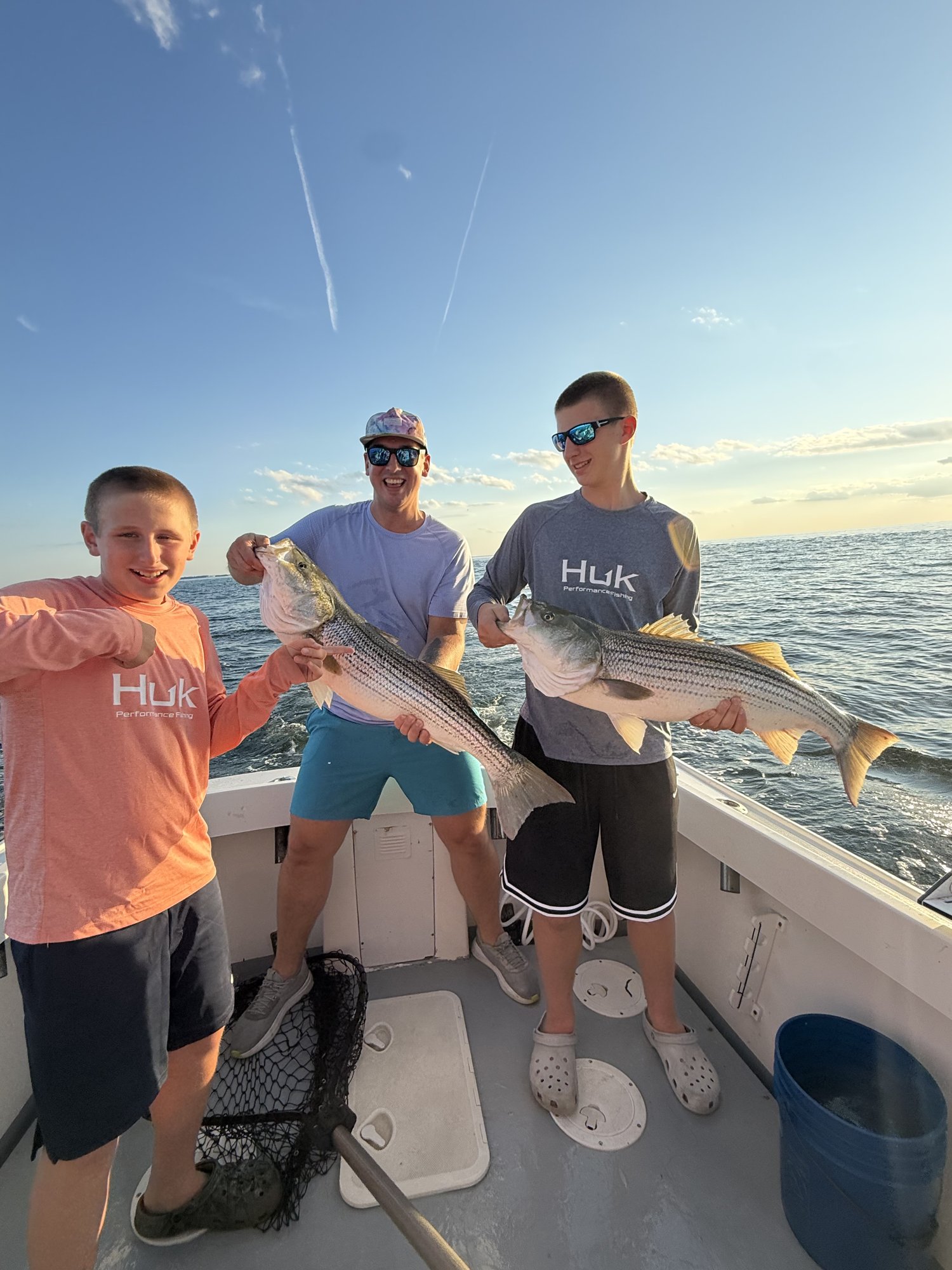 Family with a young angler holding a striped bass at sunset on the Long Island Sound