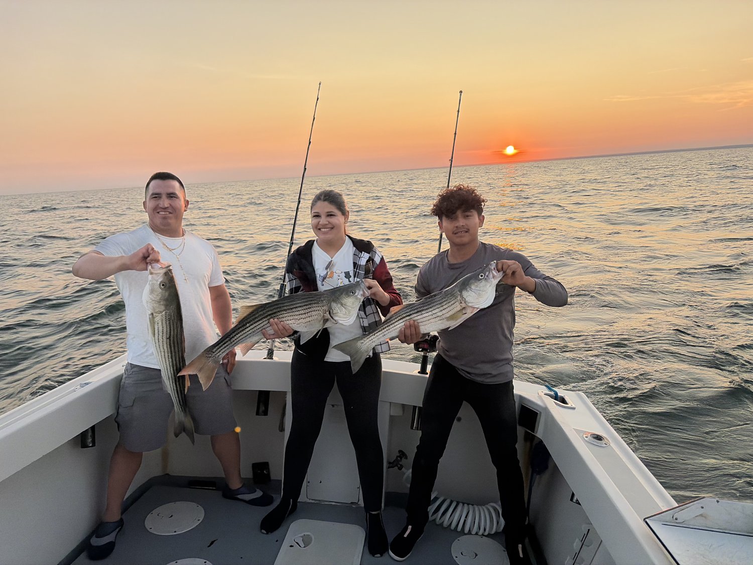 Three anglers with striped bass against a fiery Long Island Sound sunset