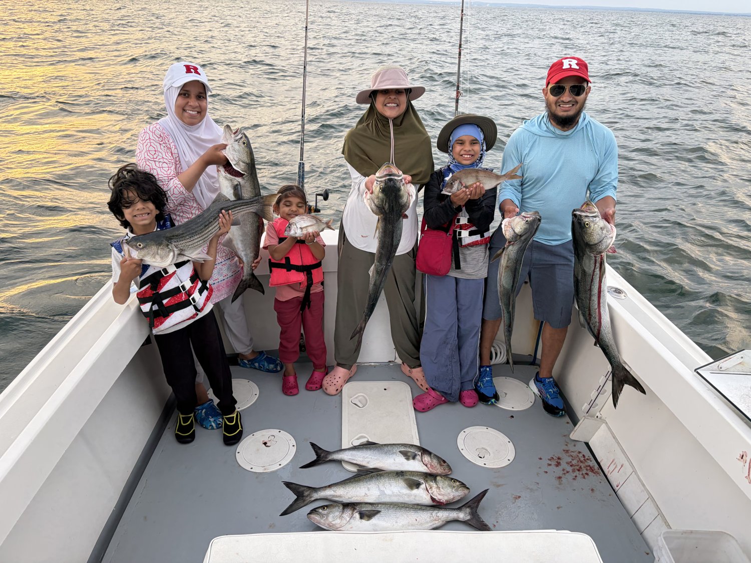 Multi-family charter with kids and adults holding a mixed catch of striped bass and bluefish on the Long Island Sound