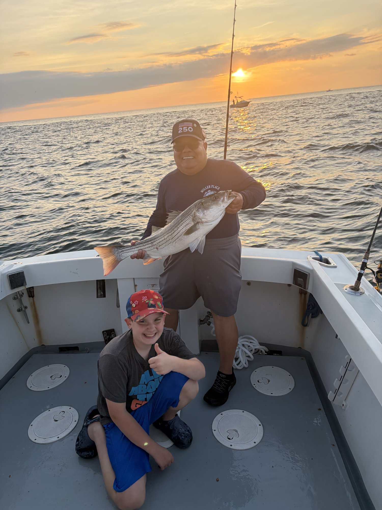 Father and son with a striped bass at sunset on the Long Island Sound aboard the Christina M II