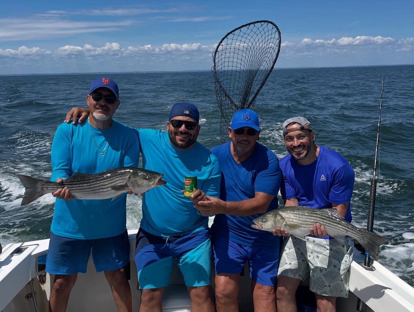 Four anglers in blue with striped bass and a landing net