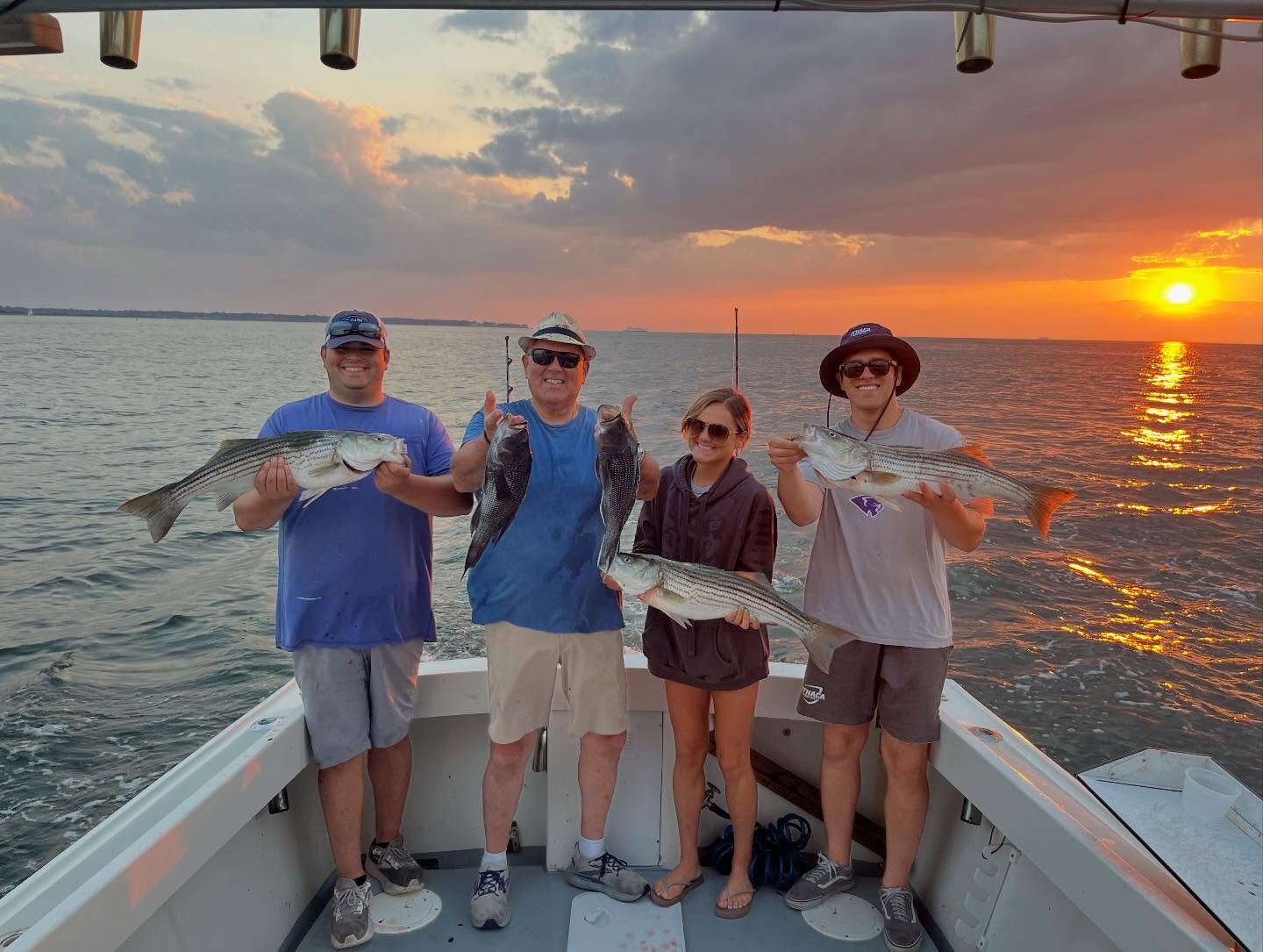 Four anglers holding stripers in front of a fiery sunset